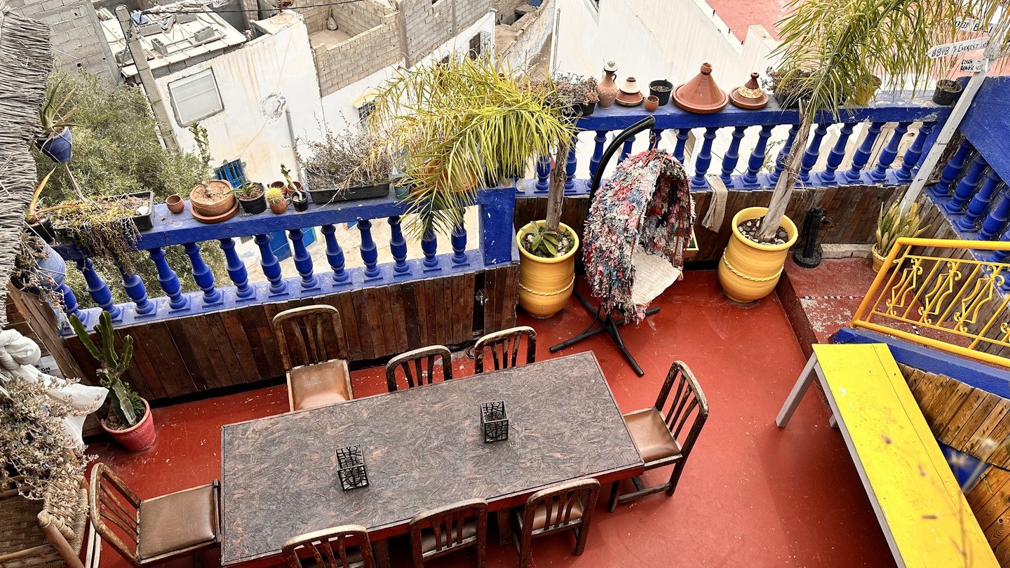 Le rooftop de Roof House à Taghazout, ses balustrades bleues, ses palmiers et la table commune